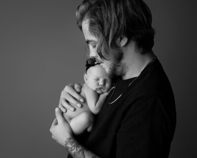 tattood dad snuggling his newborn baby during photoshoot