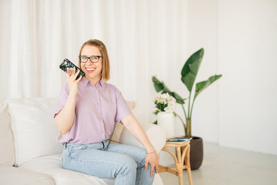 Stephanie Pampel records a voice memo for a student while sitting on a white couch.