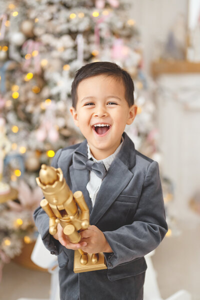 Child in holiday suit holding a gold nutcracker posing in a nutcracker-themed mini session Phoenix.