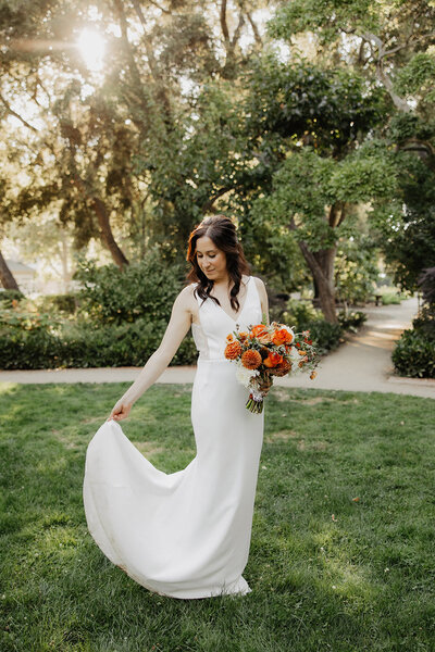 Bride in white gown holding orange wedding bouquet in garden