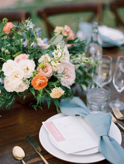 Close up of a wedding reception table setting with colorful florals and blue napkins