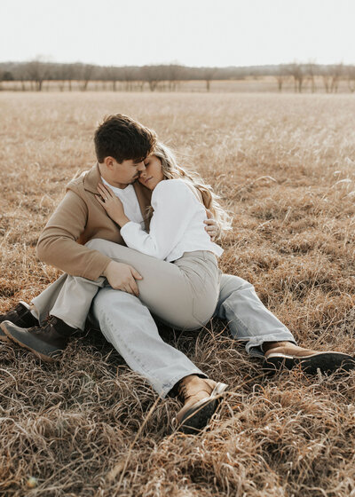 woman cuddles in her partner's lap while sitting in golden field