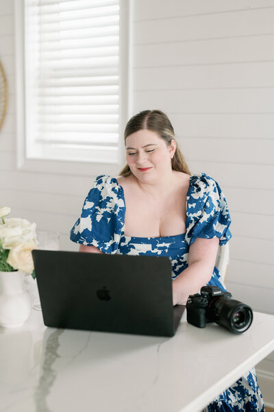 Picture of Caitlin Wilcox of Caitlin Wilcox Photography working on a grey Macbook with camera next to it