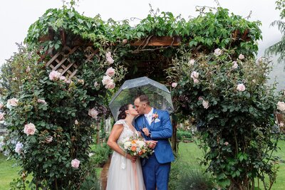 Bride and groom kissing under umbrella on rainy wedding day