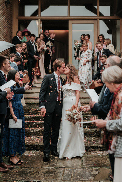 Newly weds kissing under confetti after their wedding at Bury Manor Barn