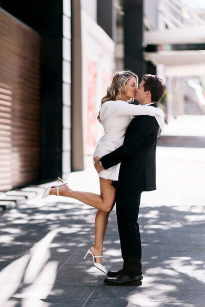 Groom lifts bride for a kiss in Brisbane city street after registry wedding ceremony