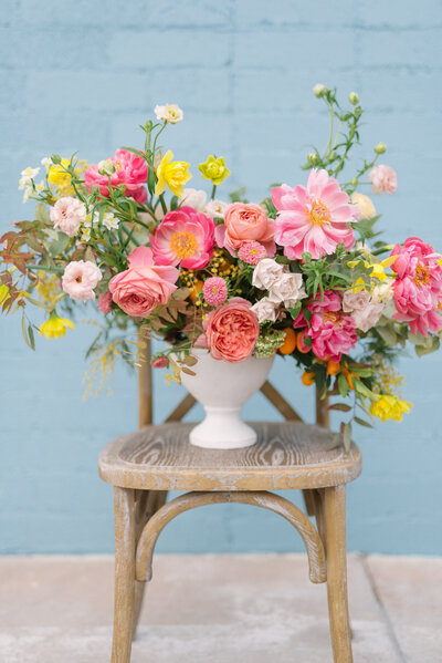 A gorgeous bouquet of pink flowers in a white case placed on a rustic chair in front of a light blue wall outside of The Doyle in Las Vegas, Nevada.