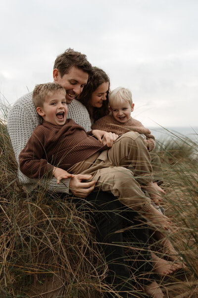 A family laugh and cuddle in the sand dunes on Banthm Beach, Devon