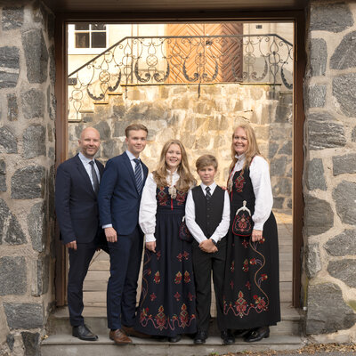 Familie i bunad poserer foran vakker steinport under fotografering nær Oslo.
