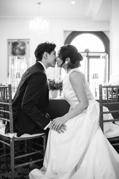 Les mariés s’étirent doucement l’un vers l’autre pour s’embrasser pendant la réception, instant tendre et spontané capturé dans l’ambiance chaleureuse d’un mariage empreint d’amour