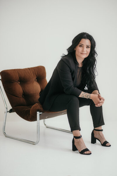 Professionally styled woman sits on a chair.