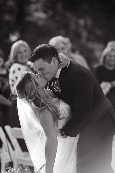 Black and white photo of a bride and groom kissing at the end of the aisle at Mountain View Ranch.