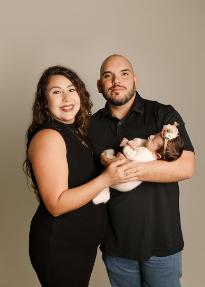 Parents standing smiling holding newborn baby in studio by Ashley Nicole in Temecula, CA.