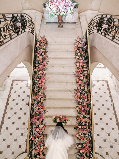 Bride walking up stairs decorated with flowers at Belmont House