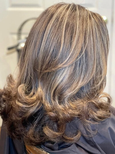 A woman with long, wavy hair featuring a beautiful balayage technique, blending from darker roots to lighter, sun-kissed ends.