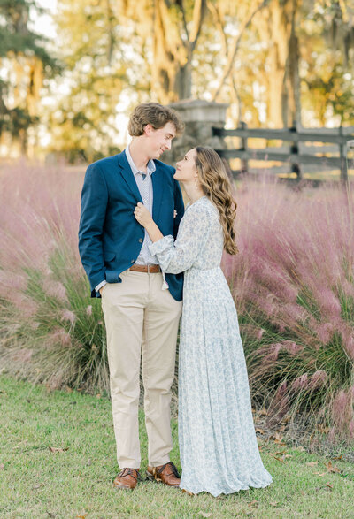 Engaged couple standing with pink grasses cuddled closely