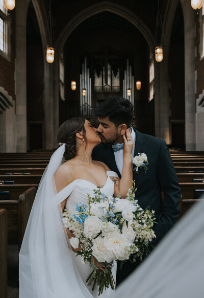 Photographer Knoxville TN photographs chapel wedding with couple kissing in the aisle with pews on either side of them and modern gothic styled lanterns overhead for a Knoxville wedding