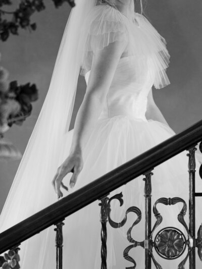 A bride runs her hand up a staircase rail in her designer wedding gown.