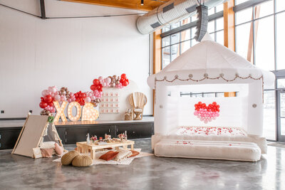 An indoor Valentine's Day picnic setup with a white bounce house and pink balloons