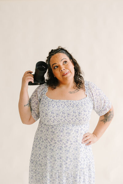 A person with a camera resting on their shoulder and the other hand on their hip