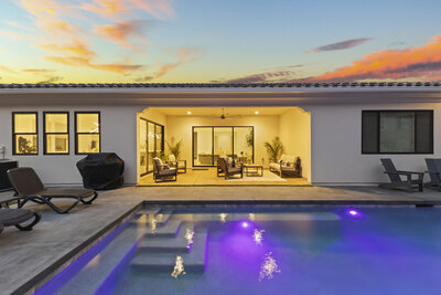 Backyard with pool and a view inside the home with lights on at twilight
