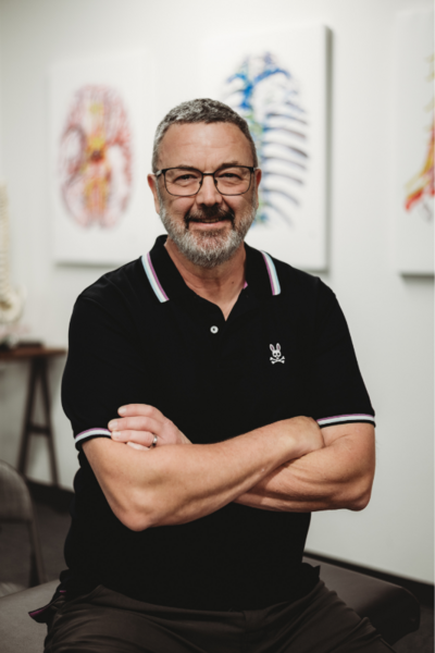 Brand photography of a male physical therapist posing confidently on a treatment table in his office
