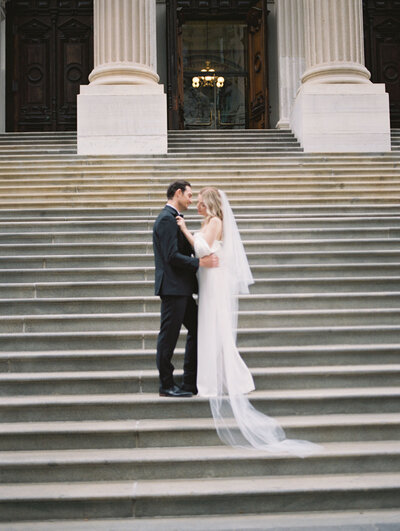 Newlyweds celebrating their elegant wedding exit on the grand steps of New York City Hall, surrounded by loved ones tossing confetti, captured by Stephanie Michelle Photography, a luxury wedding photographer specializing in timeless NYC elopement celebrations