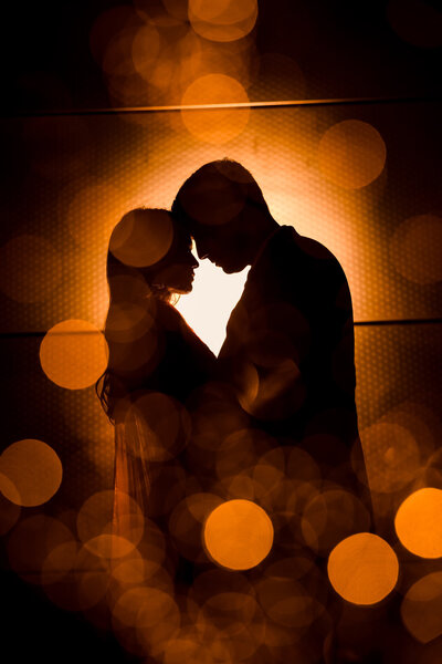 Silhouetted couple framed by golden bokeh and warm light in a dramatic NYC evening portrait, created by NYC wedding photographer Heritage House.