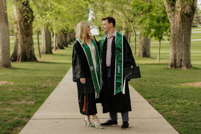 Two Colorado State University graduates smile at each other during their grad session on The Oval in Fort Collins, Colorado.