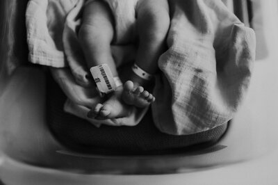 Close-up of newborn baby’s feet resting on a blanket, both wearing hospital ID bands.