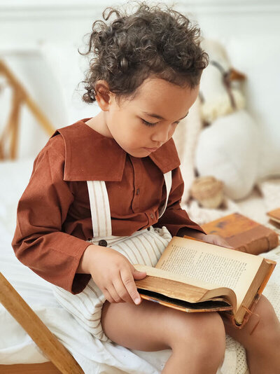 Petit garçon métisse, tenue rétro et salopette, lisant un vieux livre.