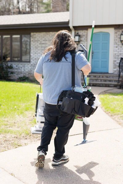 Professional cleaner walking up to house carrying cleaning supplies