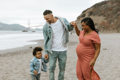 Lifestyle family photo of a mom and 5 year old son running toward the ocean on the beach in San Francisco, California. The photographer caught the photo of them in action while they are enjoying running towards the waves. The sun has set with there still being a bit of light left.