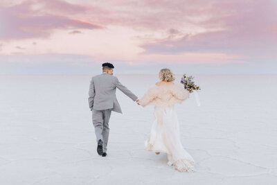 A bride and groom hold hands and run into the sunset while atop the hardened white surface of the Bonneville Salt Flats near Utah. 