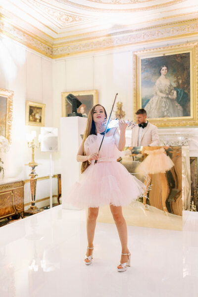 Image of an electric violinist in a pink tulle dress performing at Somerley House after-party, with a DJ in the background.