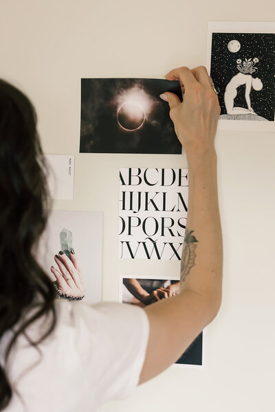 Moonstone founder Miranda arranging a mystical mood board with eclipse photography, crystal imagery, gothic serif typography, and cosmic illustrations for branding inspiration.