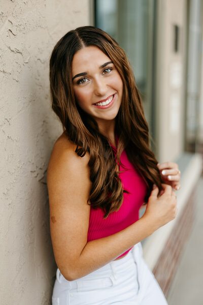 Close up portrait of a senior girl in a pink top leaning against a wall
