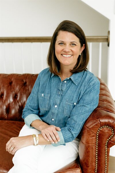 Katy Taylor Jacobson, website copywriter for wedding professionals, sitting on leather sofa.