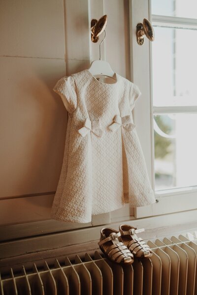 White baby dress and tiny shoes displayed by a sunlit window, symbolizing anticipation, hope, and the loving home adoption provides.