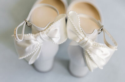 Luxury wedding photography detail of bride's shoes with a satin white bow lined with pearls