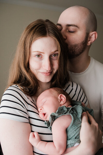 Infant photography in home, simple photo mom holding infant with dad kissing forehead
