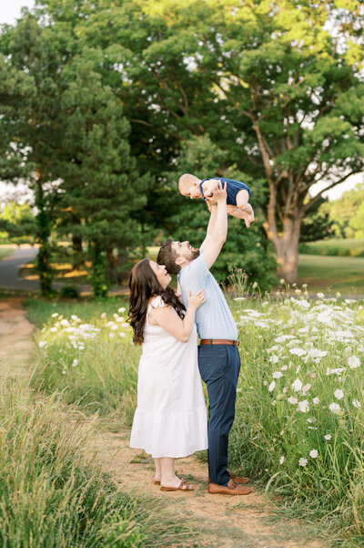 Dad holds baby boy in the air while mom looks over his shoulder for photos in Raleigh North Carolina