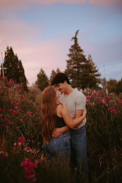 man and woman embracing while standing in field of trees and flowers