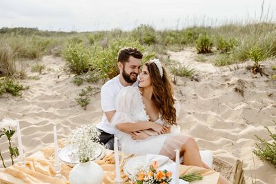 Bride and groom sit on the beach at a luxury picnic during