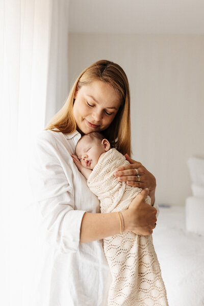 A mother holding a baby and rocking her in her arms while she's photographed candidly by lucy jane photography in her christchurch newborn photography studio