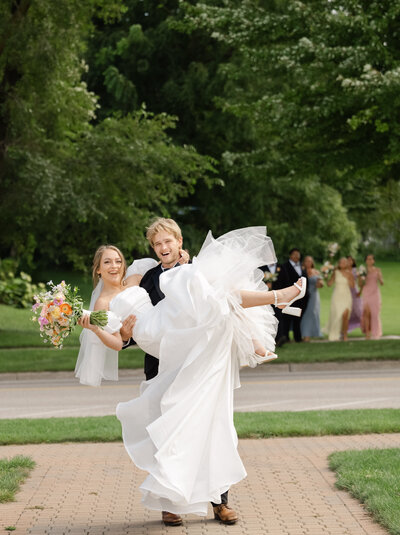 A groom holds his bride as they laugh in front of their wedding party.