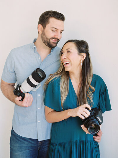 Shelby and Jared holding cameras while smiling at each other