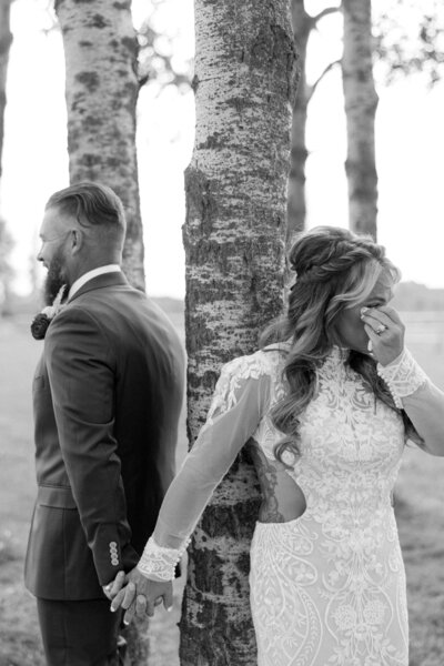 Black and white photo of bride and groom holding hands while facing away during their first look.