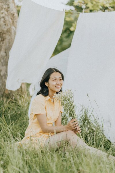 Girl in yellow dress sitting in green grass holding chamomile