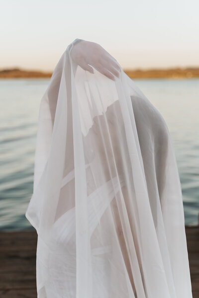 Ethereal white wedding veil flowing gently in the breeze against a serene waterfront backdrop at sunset, capturing the romantic Pacific Northwest lakefront atmosphere near Portland, Oregon, in a dreamy wedding photography style